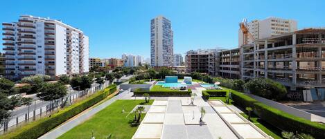 Un área urbana moderna con edificios altos, una plaza central con piscina y abundante vegetación.