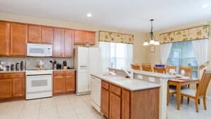 A kitchen with wooden cabinets, a white stove, a microwave, and a refrigerator. There is a dining area with a table and chairs. - Tigerlilly Private Pool Villa (Davenport)