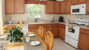 A kitchen with wooden cabinets, a white stove, a microwave, and a dining table with chairs. - Ic018or (Kissimmee)