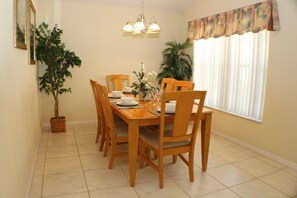 A dining area with a wooden table and chairs, a chandelier, and a window with curtains. - Ic018or (Kissimmee)