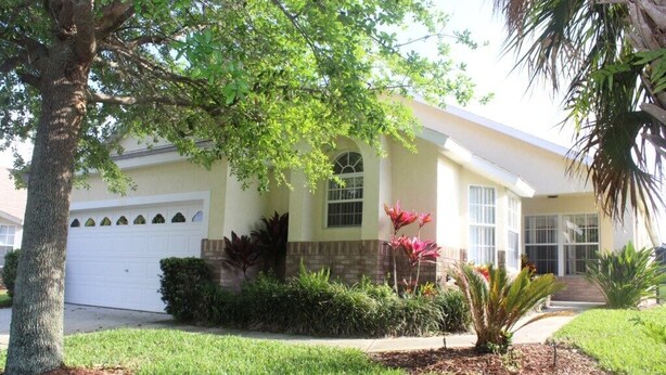 A single-story house with a white garage, surrounded by well-maintained lawns and various plants. - Ic018or (Kissimmee)