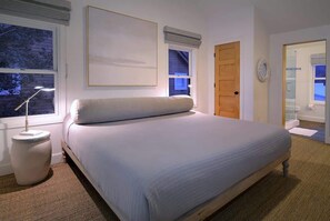 A bedroom with a bed, bedside lamp, window, door, and a mirror.