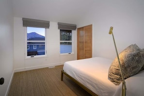 Ein Schlafzimmer mit einem Bett, zwei Fenstern, einer Tür und Blick auf einen Berg.