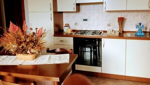 Una cocina con armarios blancos, estufa a gas y lavavajillas. Hay una mesa con un mantel individual y una planta en maceta.
