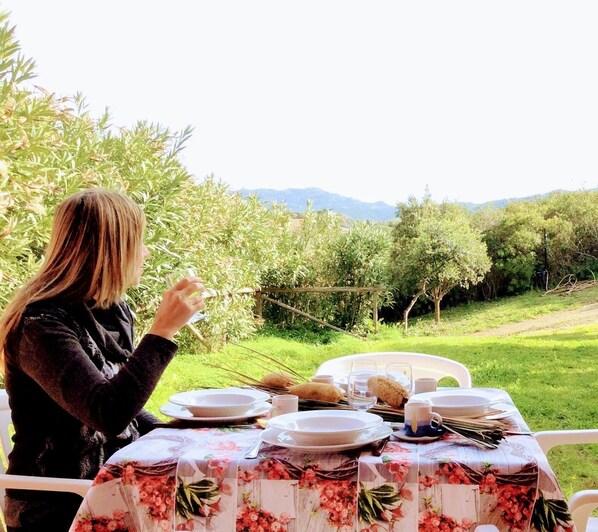A table set outdoors with a floral tablecloth, surrounded by greenery and a mountainous backdrop.
