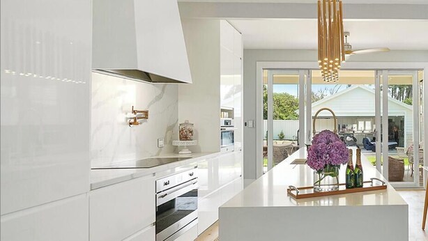 A modern kitchen with white cabinetry, a central island, and a dining area with a wooden table and chairs. - A Luxurious Beachfront Getaway  (Blacksmiths)