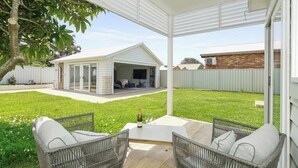 A self-contained studio unit with a covered patio, a sliding glass door, and a small outdoor seating area with wicker furniture. - A Luxurious Beachfront Getaway  (Blacksmiths)