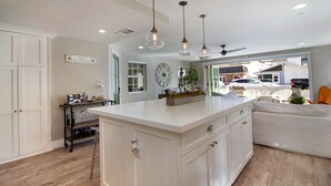 A spacious kitchen with a large island, pendant lights, and a view of the backyard. - Indoor/Outdoor Living with Stackable Doors, Firepit, BBQ, Outdoor Heater & More! (Newport Beach)