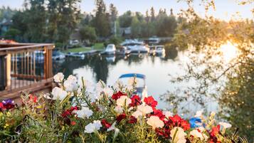 Uitzicht op het water met boten, een houten steiger en kleurrijke bloemen op de voorgrond.