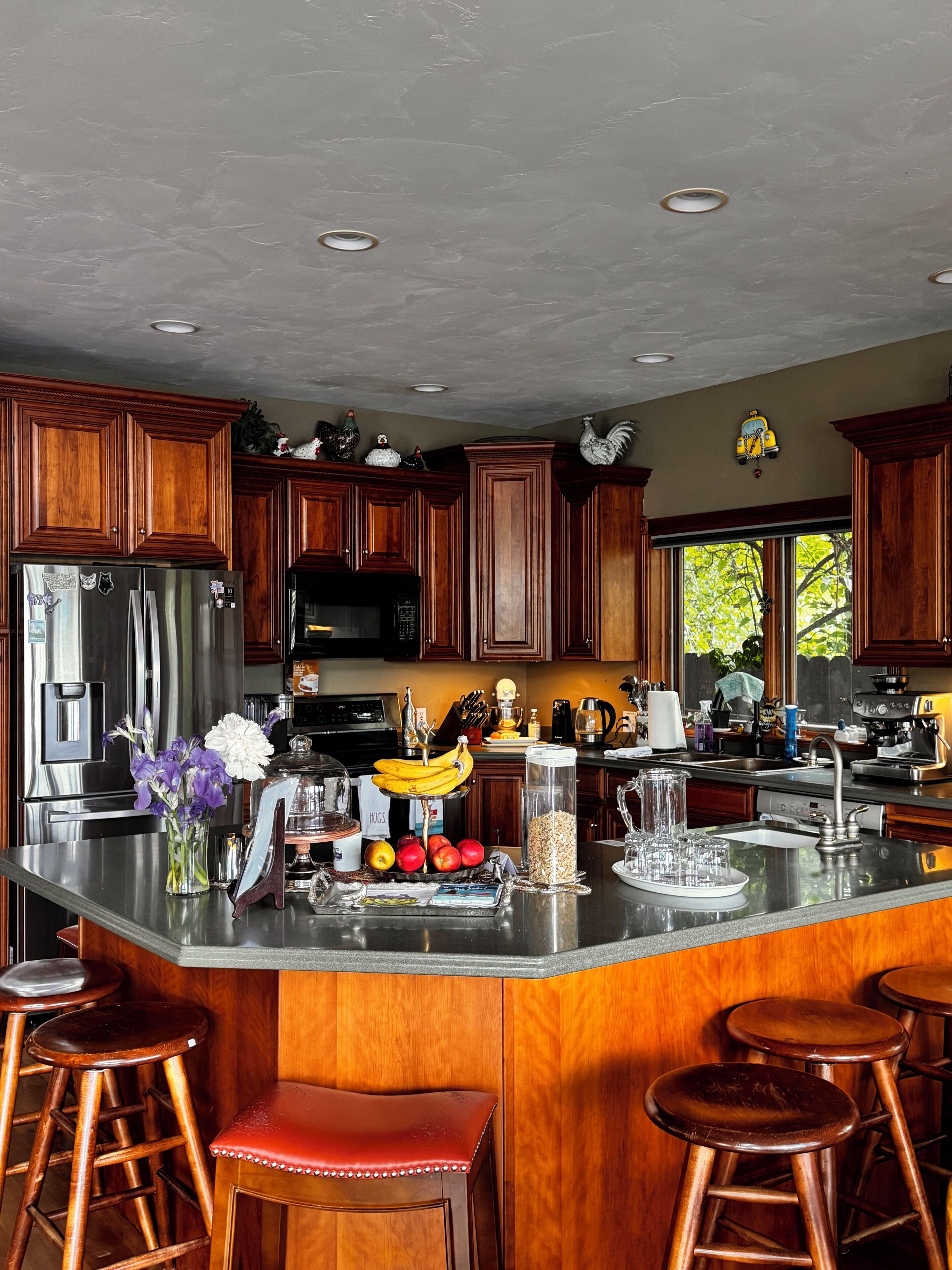 A kitchen with wooden cabinets, stainless steel appliances, a central island with stools, and a window with a view.