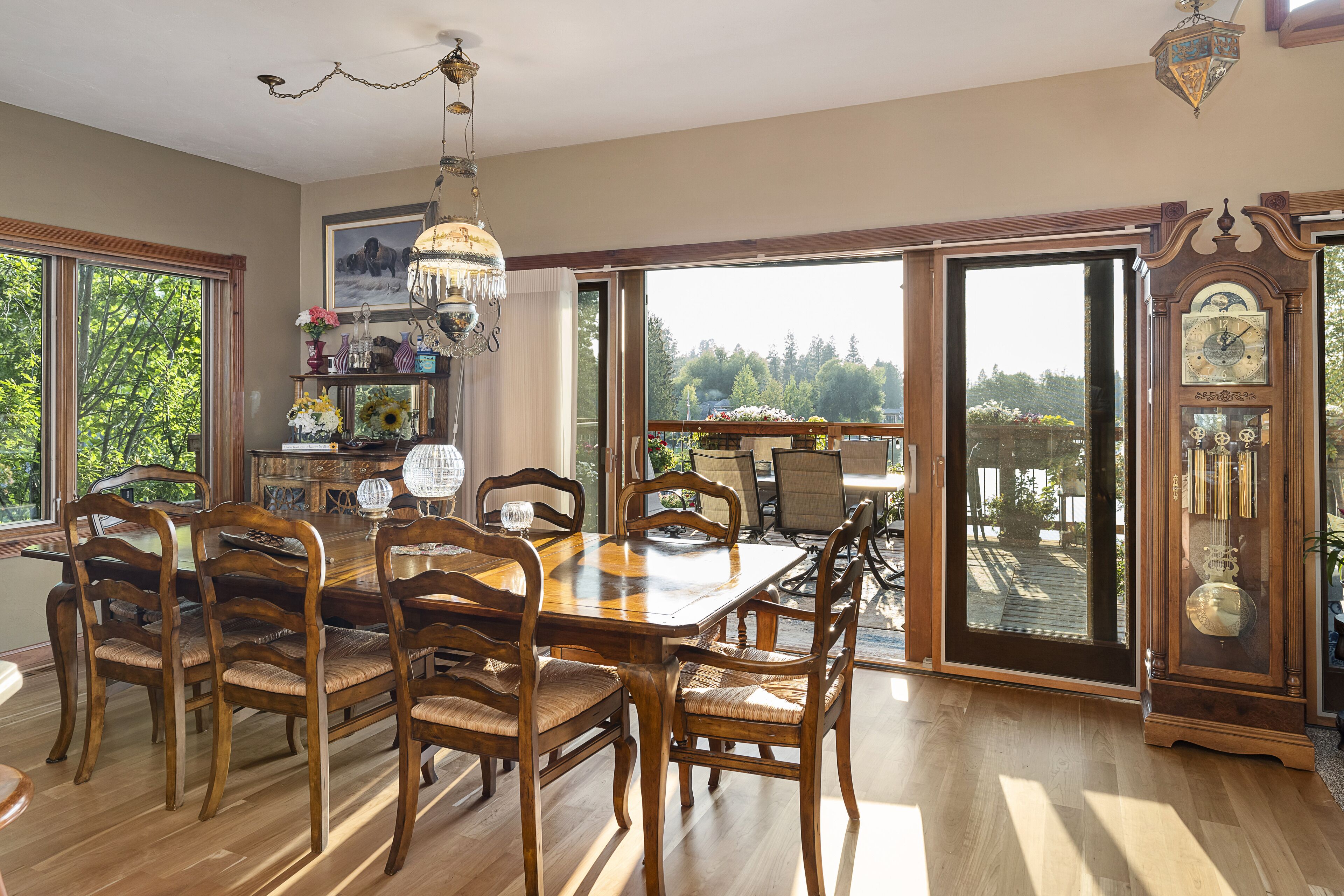 Comedor con mesa y sillas de madera, una lámpara de araña y un ventanal con vistas a árboles.