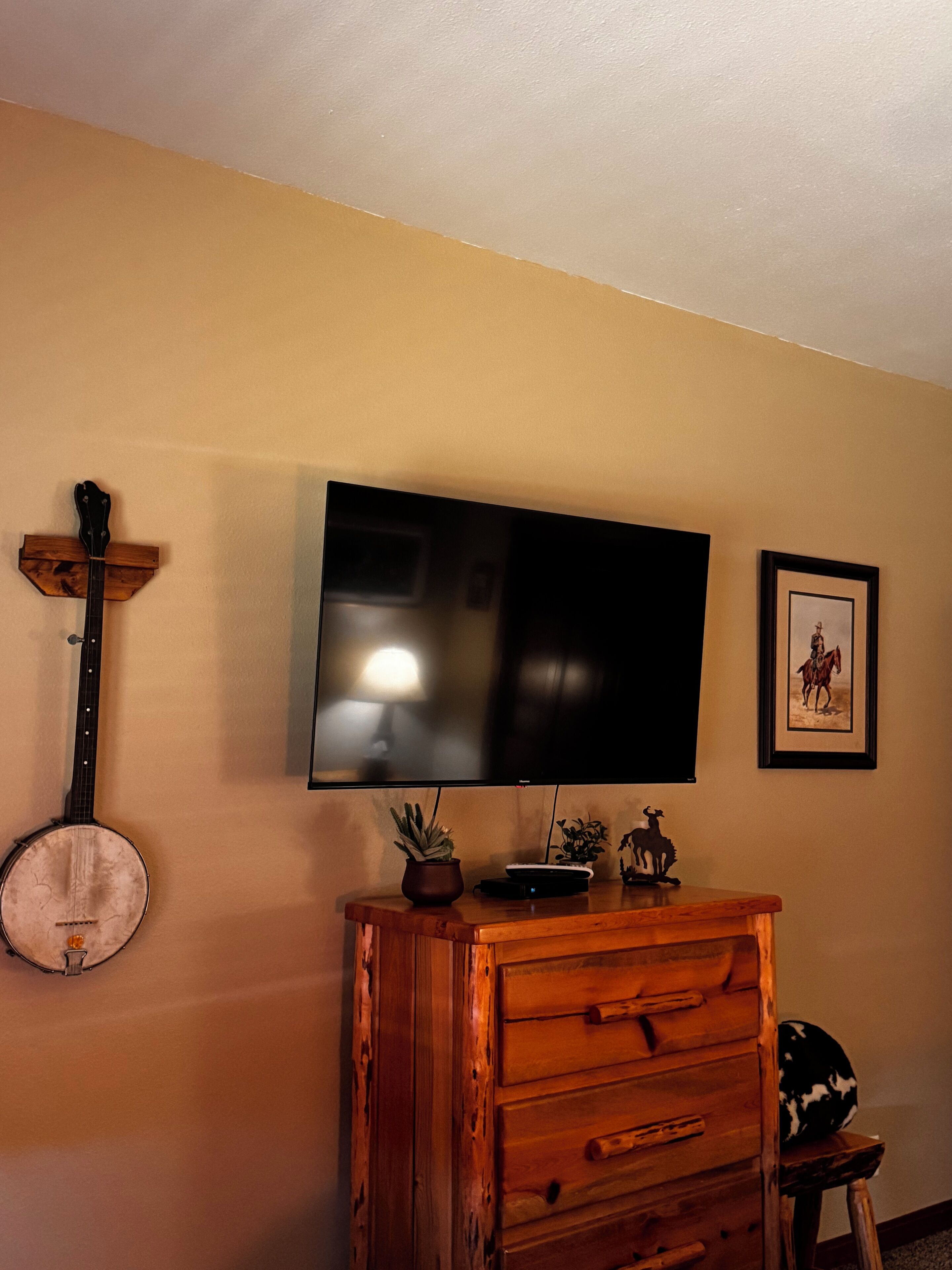 A room with a television mounted on the wall, a wooden cabinet, a banjo, and a framed picture.