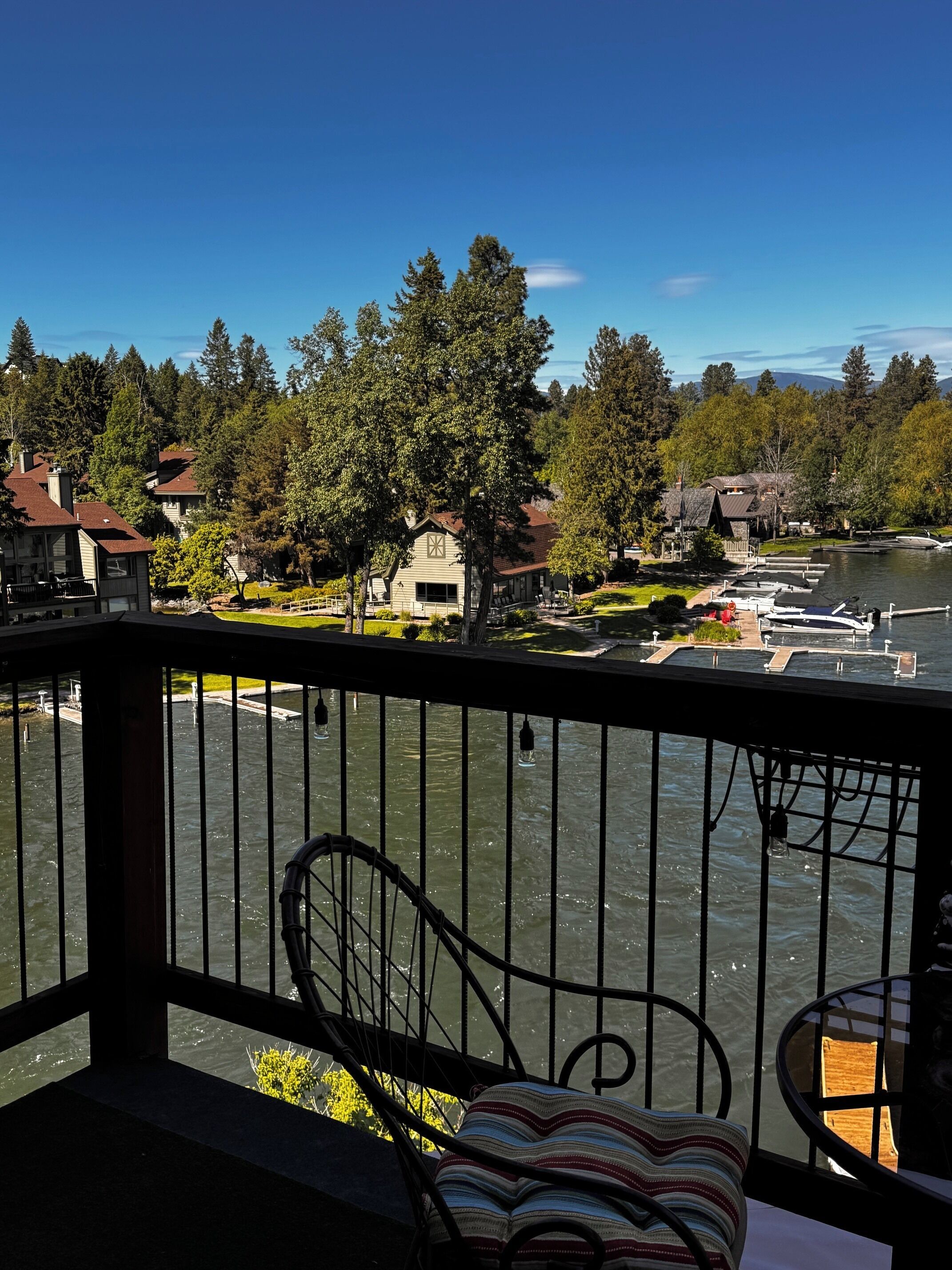 A balcony with a view of a lake, docked boats, and houses in the background.