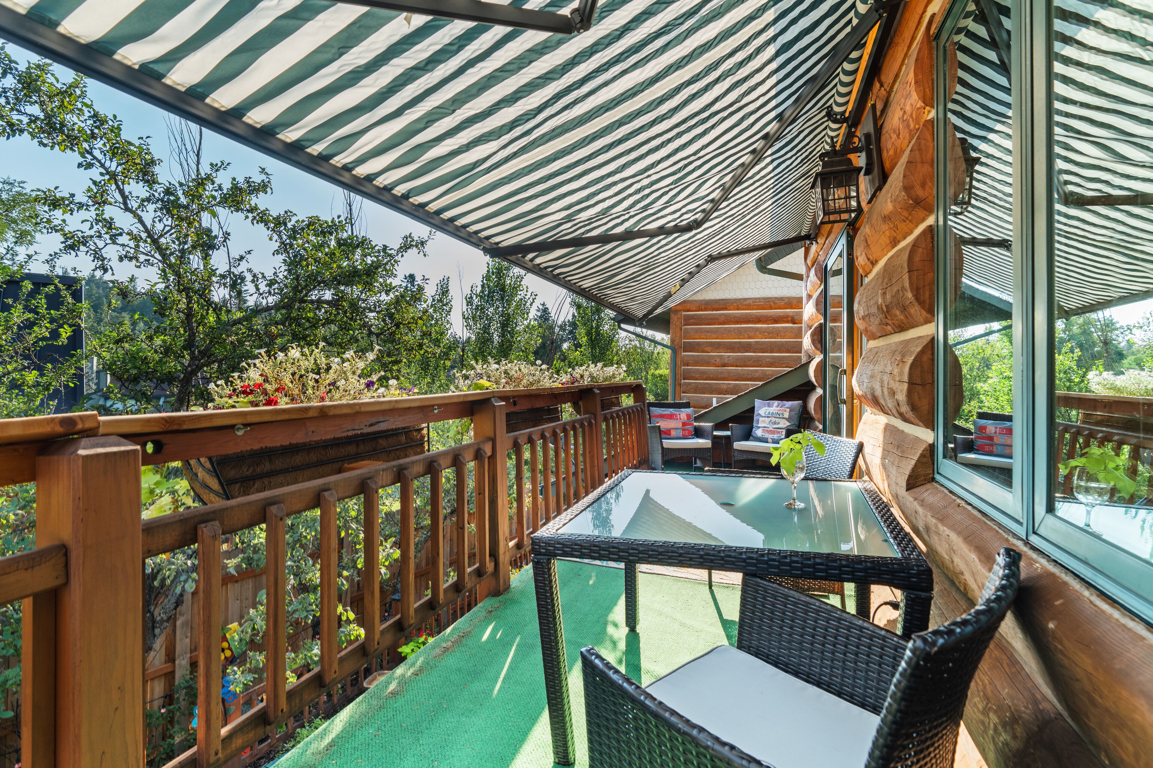 A wooden deck with a glass table and wicker chairs, surrounded by a wooden railing and a green artificial turf.