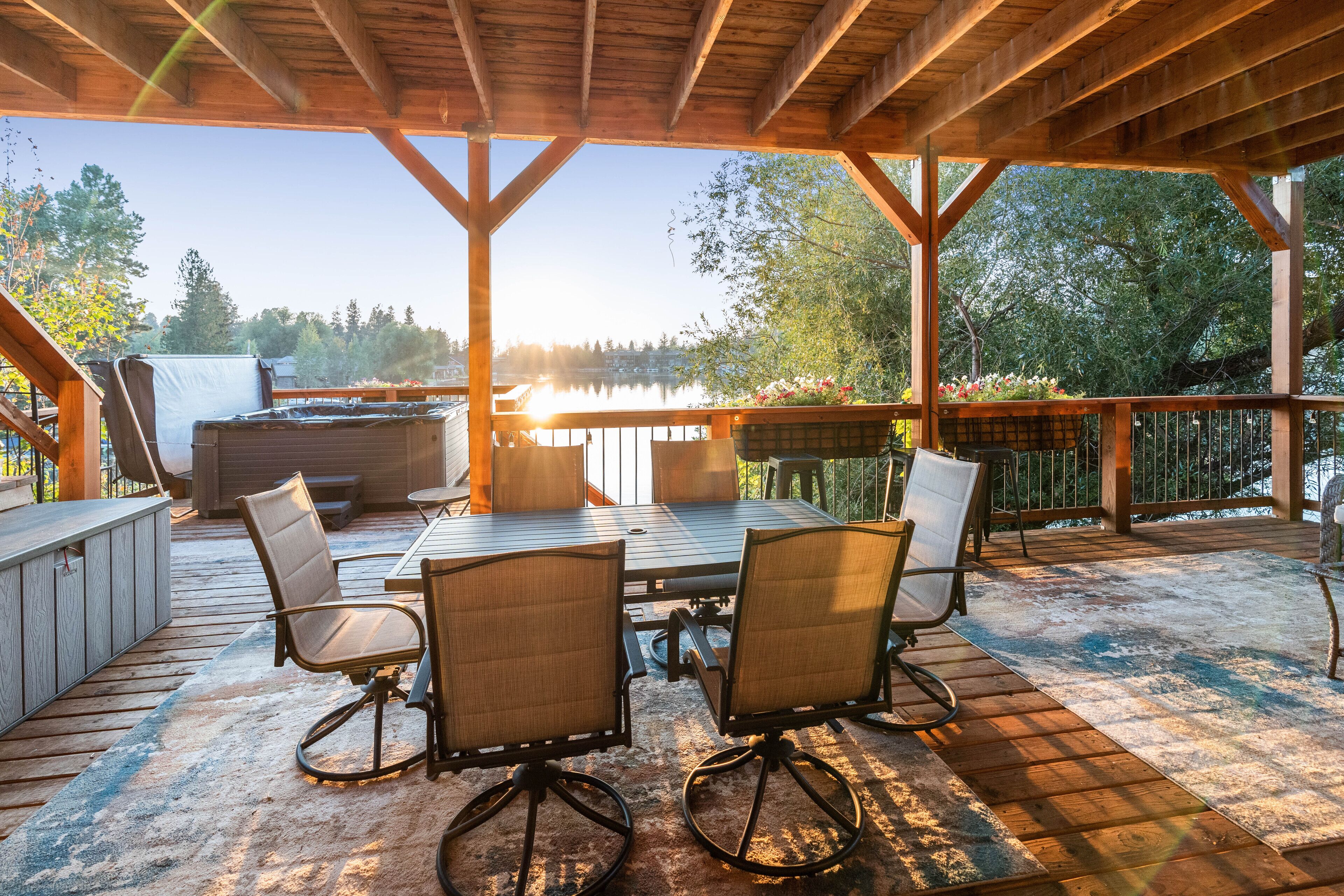 Un patio exterior con cubierta de madera, una mesa y sillas, y vistas a un lago.