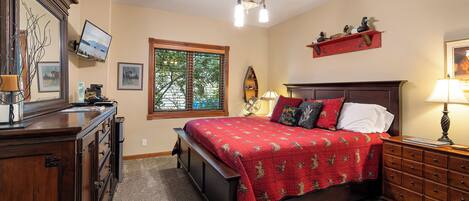 A bedroom with a large bed, wooden dresser, and a television mounted on the wall.