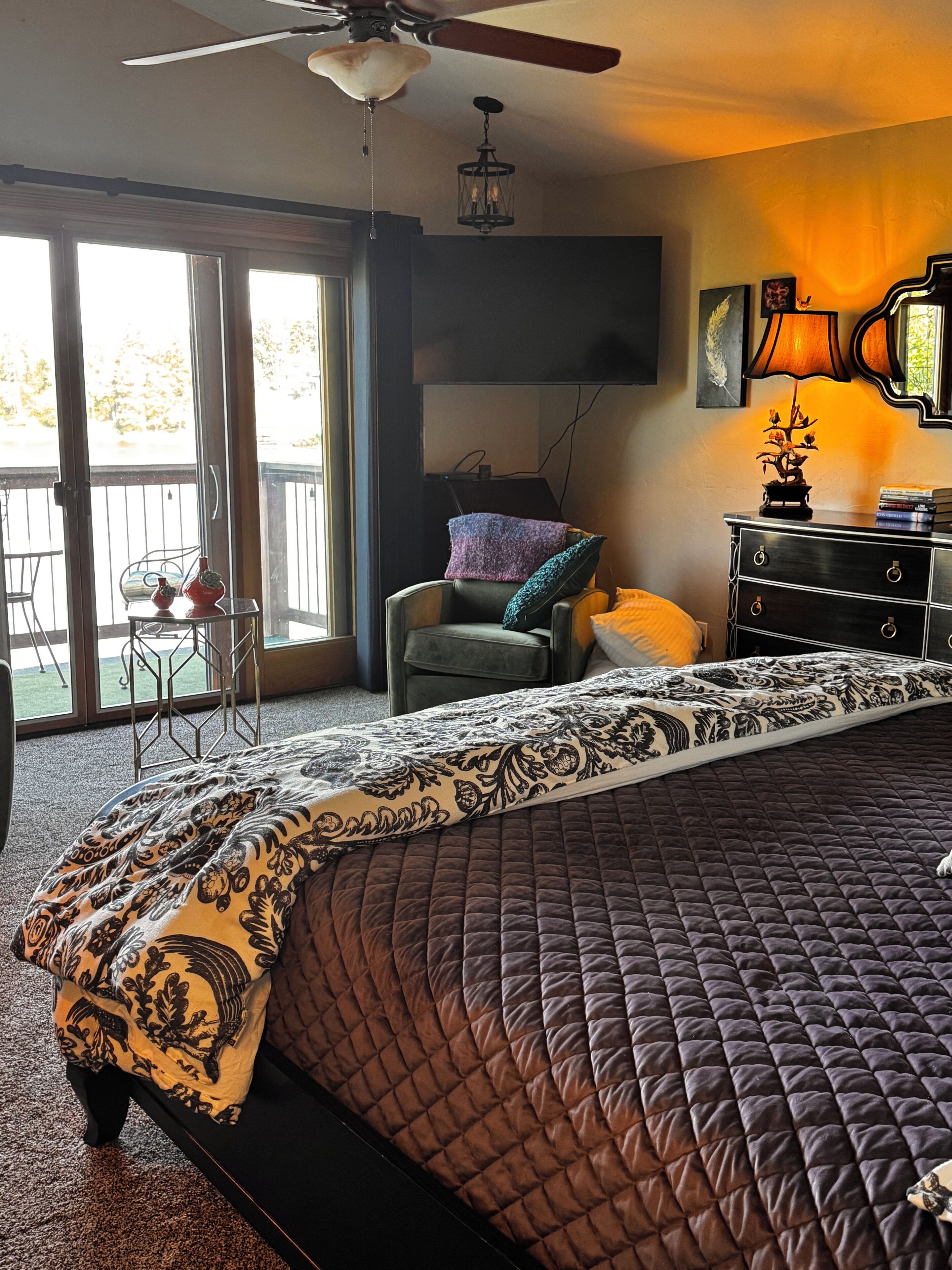 Une chambre avec un grand lit, une chaise, une table, un téléviseur et un balcon.