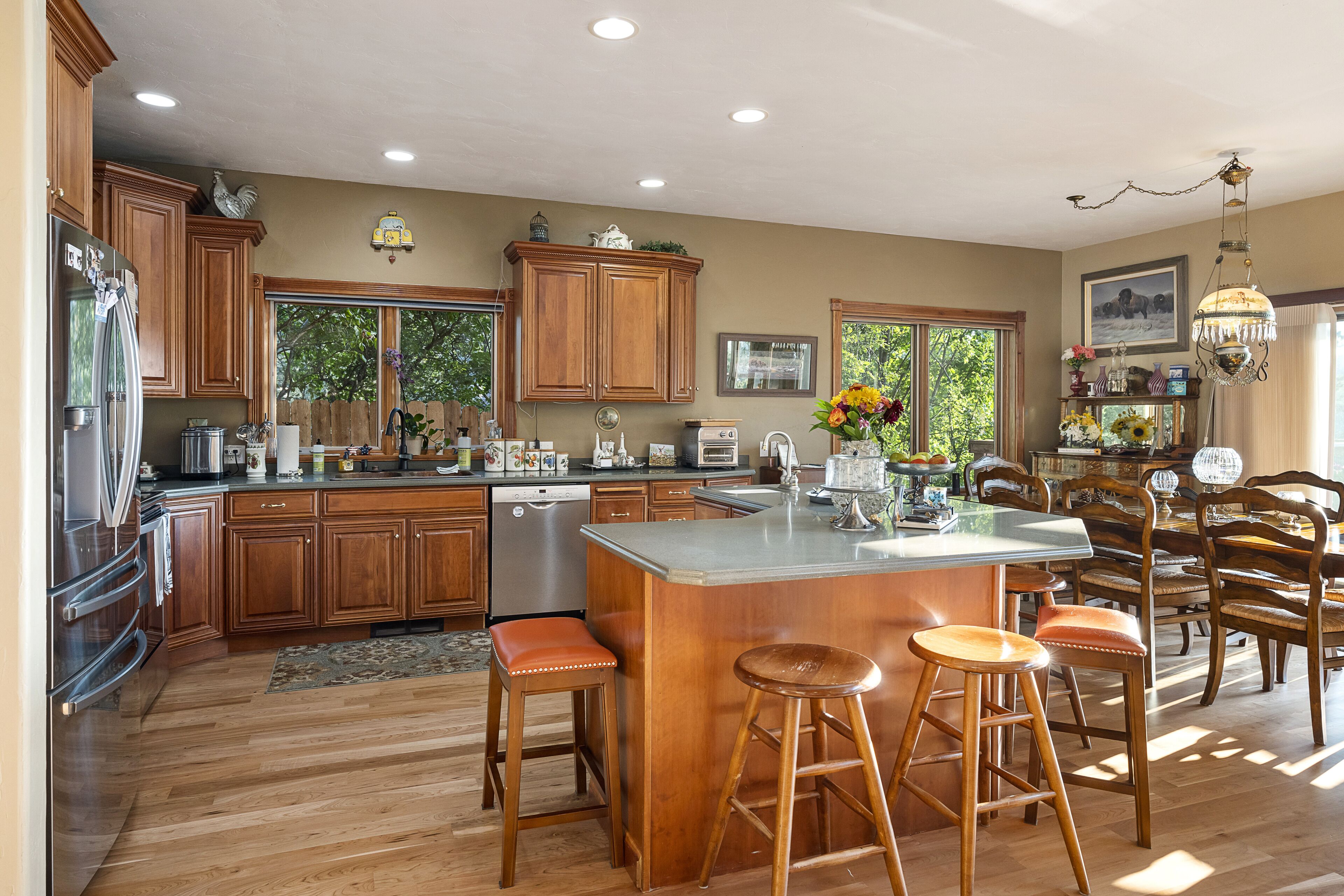 A spacious kitchen with wooden cabinets, a large island with stools, and a view of the outdoors through windows.