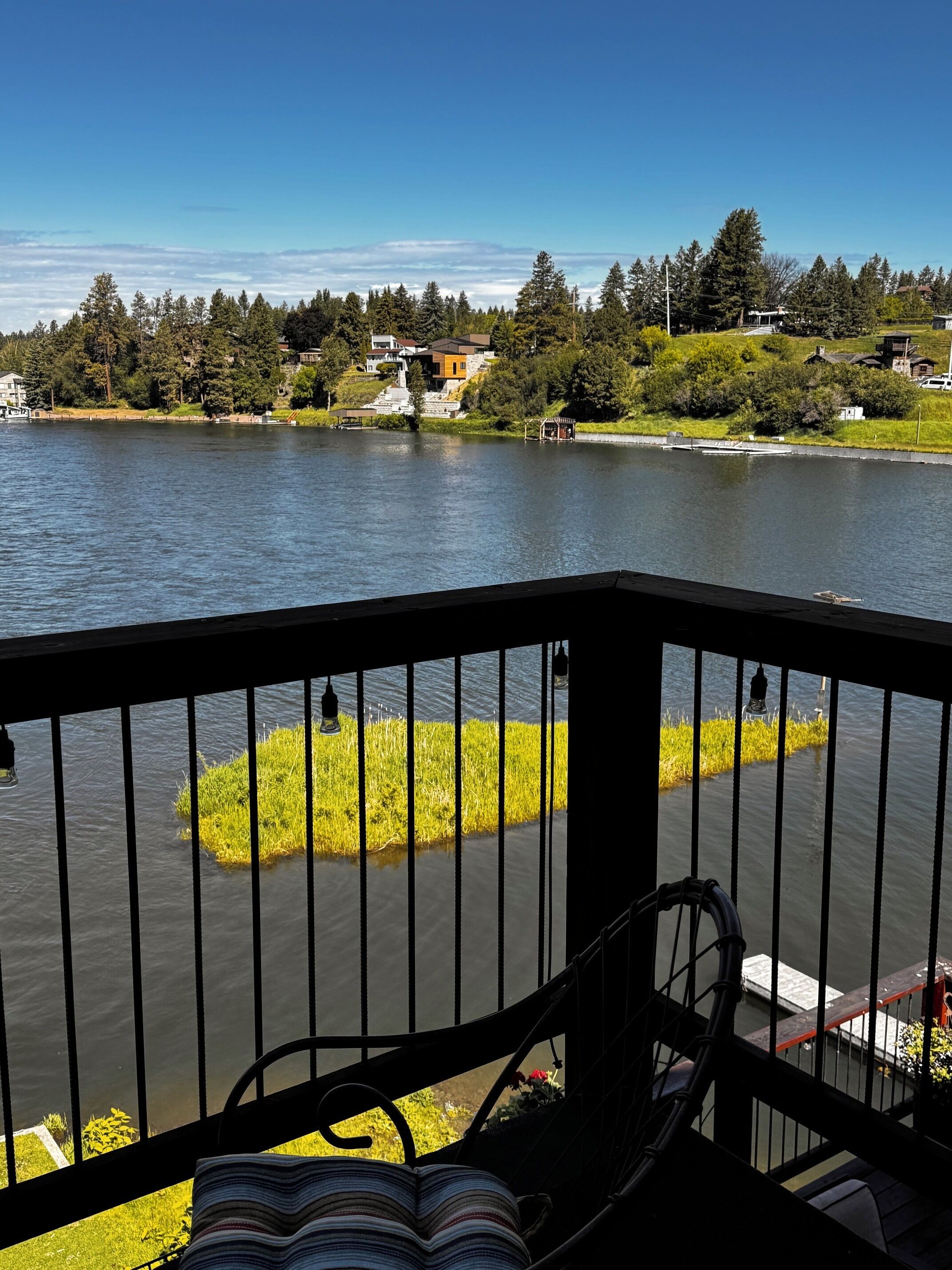 A balcony with a view of a lake, a grassy area, and houses in the background.