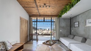 A modern living room with a wooden ceiling, a large window with a city view, a sofa, a coffee table, and a leather rug. - Ipanema Hills 7 Ensuites (Rio de Janeiro)