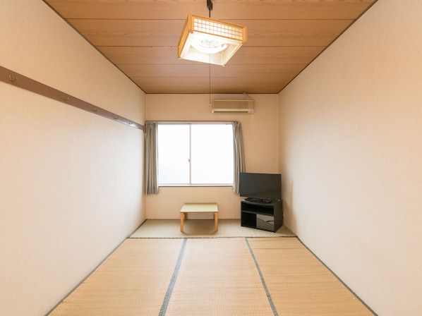 A room with tatami flooring, a sliding door, a television, and a ceiling fan.