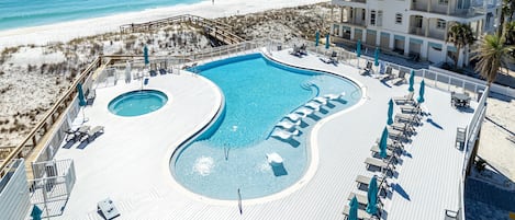 En pool på ett semesterhotell med en böjd design, omgiven av solstolar och parasoller, med utsikt över en strand och havet.