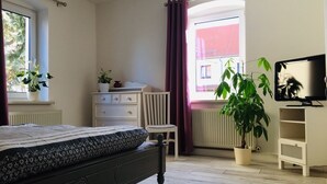 A bedroom with a bed, a dresser, a chair, a TV, and a window with curtains. - Living in a country house near Bautzen/ OT Doberschau (up to 4 persons; vacation apartment) (Doberschau)