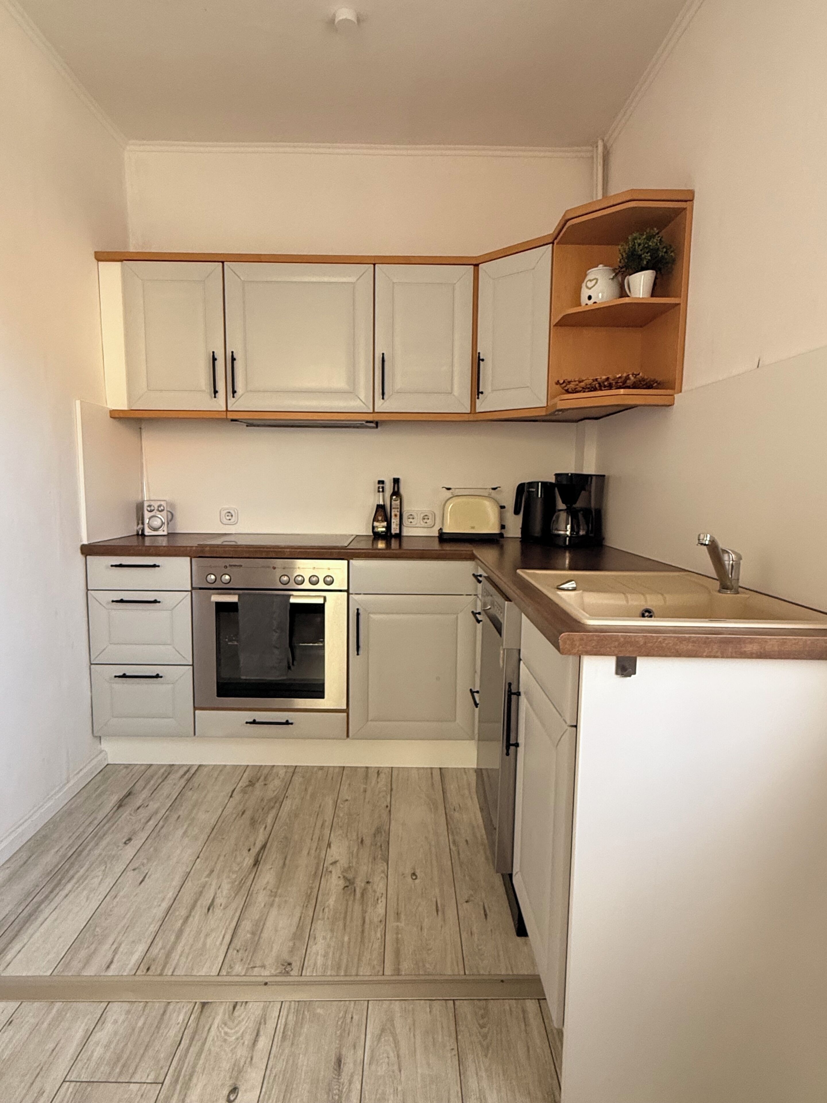 Eine kleine Küche mit weißen Schränken, einem eingebauten Backofen, einem Toaster und einer Kaffeemaschine.