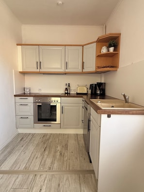 A compact kitchen with white cabinets, a built-in oven, a toaster, and a coffee maker.