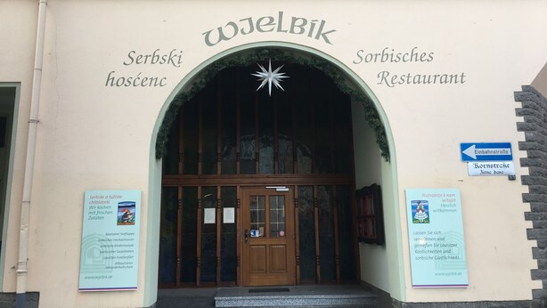 The entrance to a Serbian restaurant with a wooden door and signage in multiple languages. - Living in a country house near Bautzen/ OT Doberschau (up to 4 persons; vacation apartment) (Doberschau)