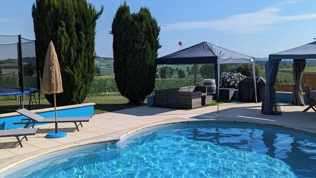 A swimming pool with lounge chairs and a covered area, surrounded by trees and a clear sky. - Gîte du Silence - Stylish gîte in beautiful French countryside (Coulx)