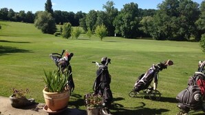 A golf course with a clear sky, trees, and golf bags in the foreground. - Gîte du Silence - Stylish gîte in beautiful French countryside (Coulx)