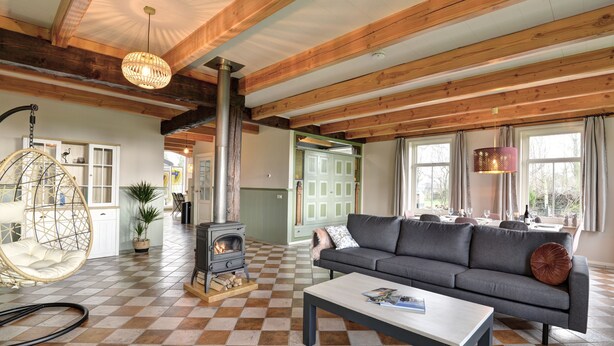 A cozy living room with a checkered floor, a sofa, a hanging chair, a fireplace, and large windows. - Stay at our beautiful farmhouse, enjoy the authentic atmosphere (Monnickendam)
