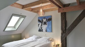 A bedroom with a skylight, a bed, a painting of a cow, and a small table with a candle. - Stay at our beautiful farmhouse, enjoy the authentic atmosphere (Monnickendam)