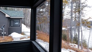 A cabin with a window view of a snowy landscape and a small shed. - Au Sable Riverview Resort (Grayling)
