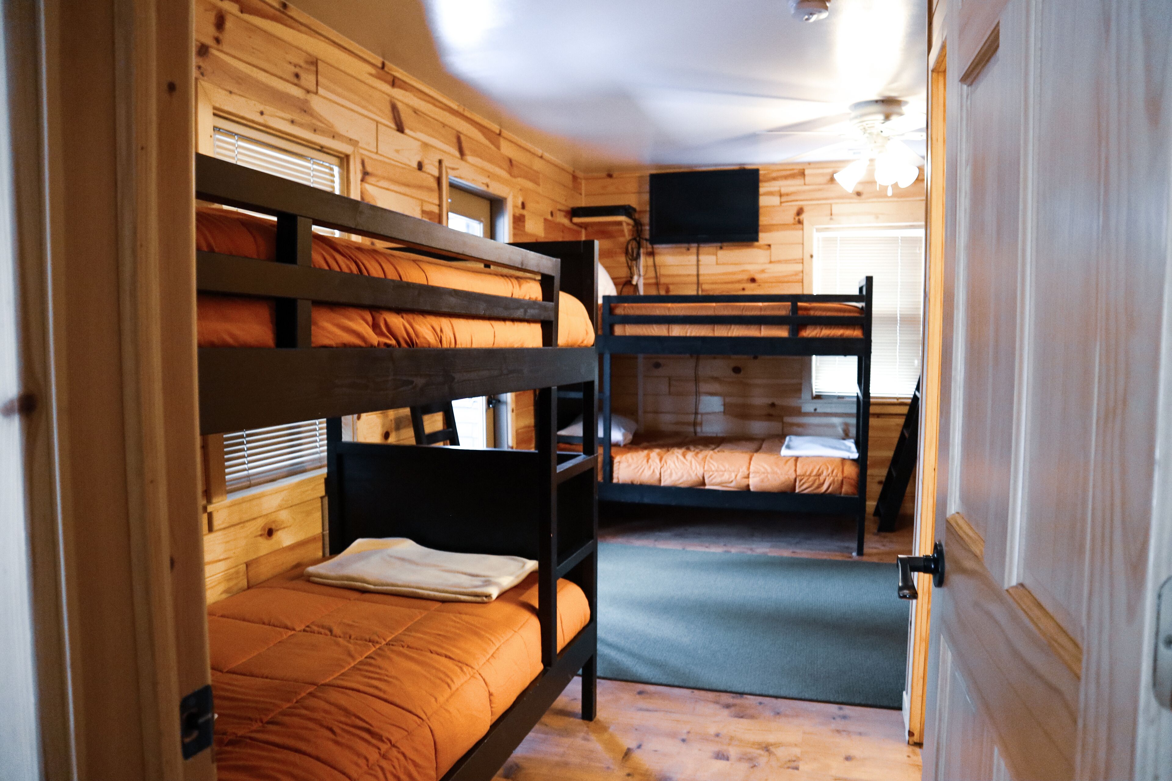 A room with bunk beds, wooden walls, a television, and a door.