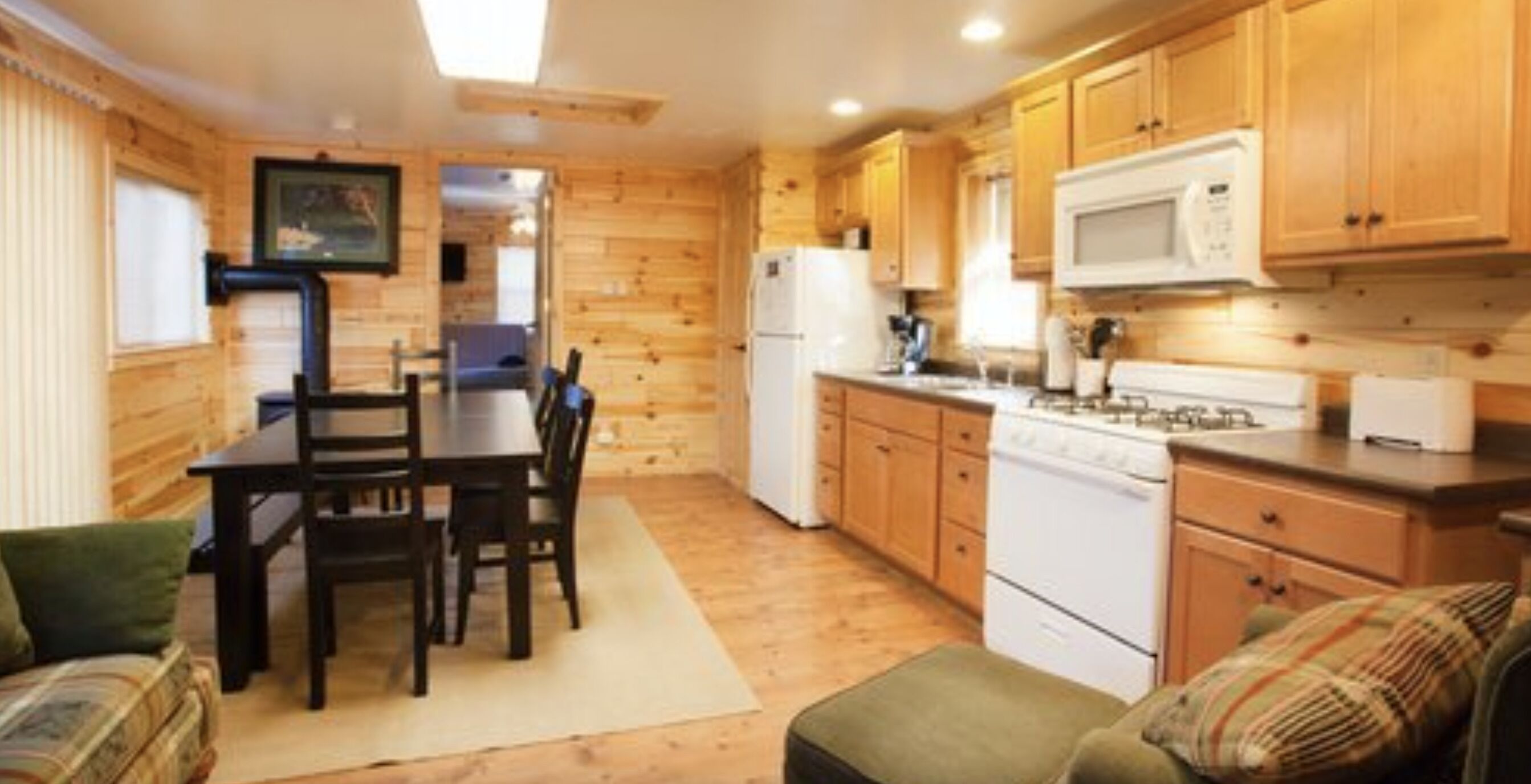 A compact kitchen with wooden cabinets, a dining table with chairs, a refrigerator, and a microwave.