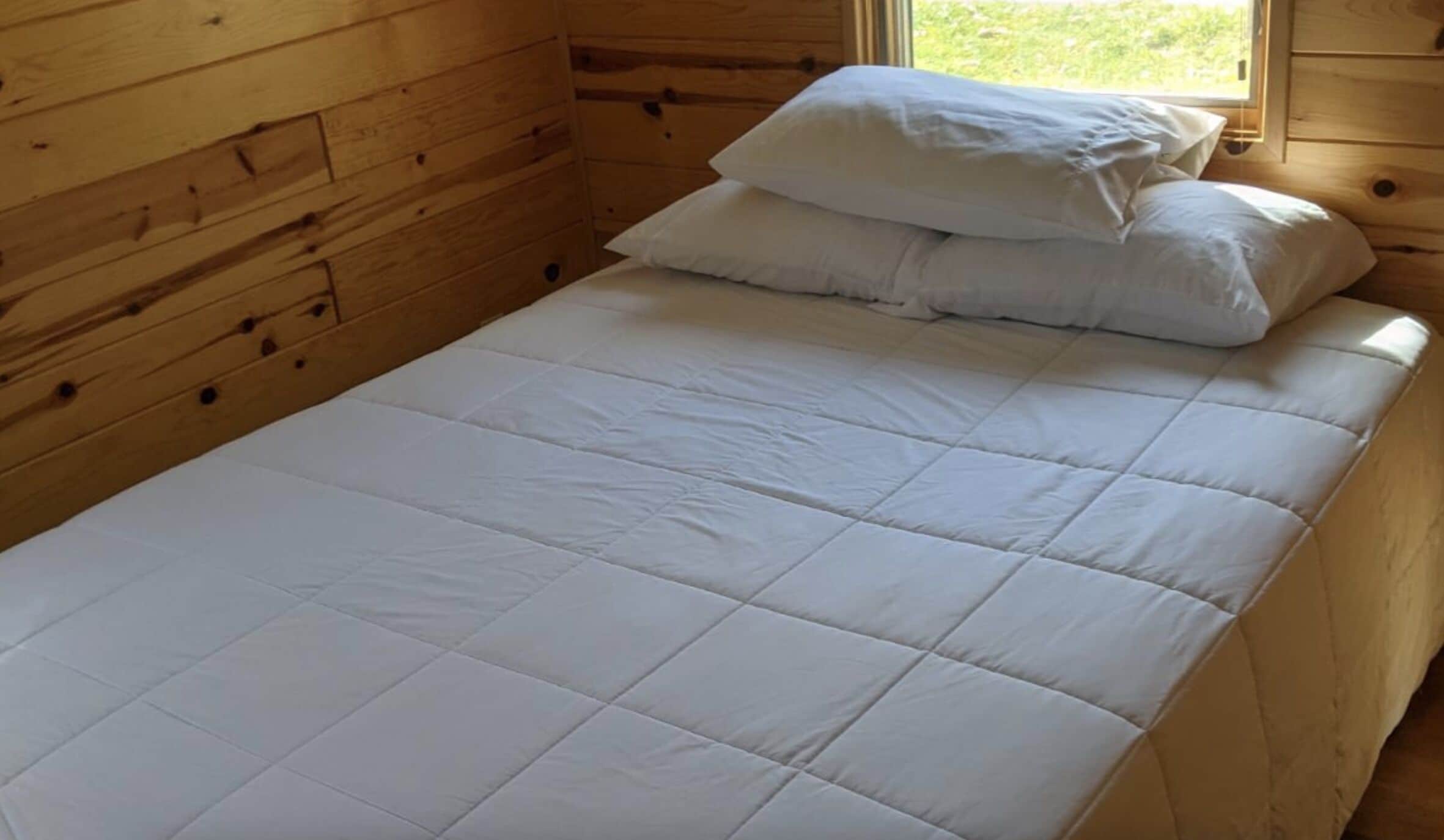 Ein Einzelbett mit weißer Bettwäsche in einem Holzhüttenraum.