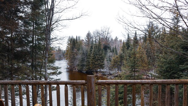 A wooden deck with chairs overlooking a river surrounded by trees. - Au Sable Riverview Resort (Grayling)