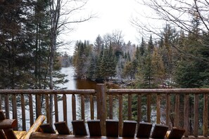 A wooden deck with chairs overlooking a river surrounded by trees. - Au Sable Riverview Resort (Grayling)