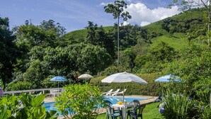 A pool area with lounge chairs and umbrellas, surrounded by lush greenery and hills. - Pousada Cruzeiro do Sul (Itatiaia)