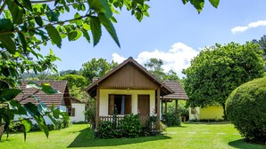 A small, single-story house with a brown roof and white walls, surrounded by a well-maintained lawn and various trees. - Pousada Cruzeiro do Sul (Itatiaia)