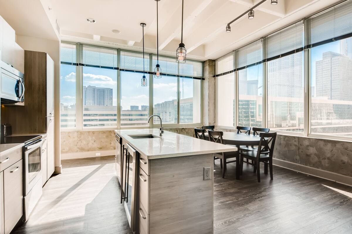 A modern kitchen with a large island, a dining area with chairs, and large windows offering a city view.