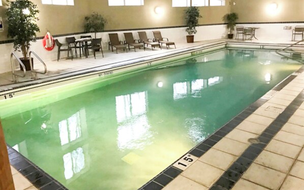 Ein Innenpool mit klarem Wasser, einer gefliesten Liegefläche, Liegestühlen und Topfpflanzen.
