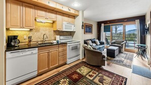 A modern kitchen with wooden cabinets, a built-in oven, and a microwave. There is a dining area with a sofa and a view of the outdoors. - Cozy Wildernest Retreat w/ Mountain Views + Pool & Hot Tub (Silverthorne)