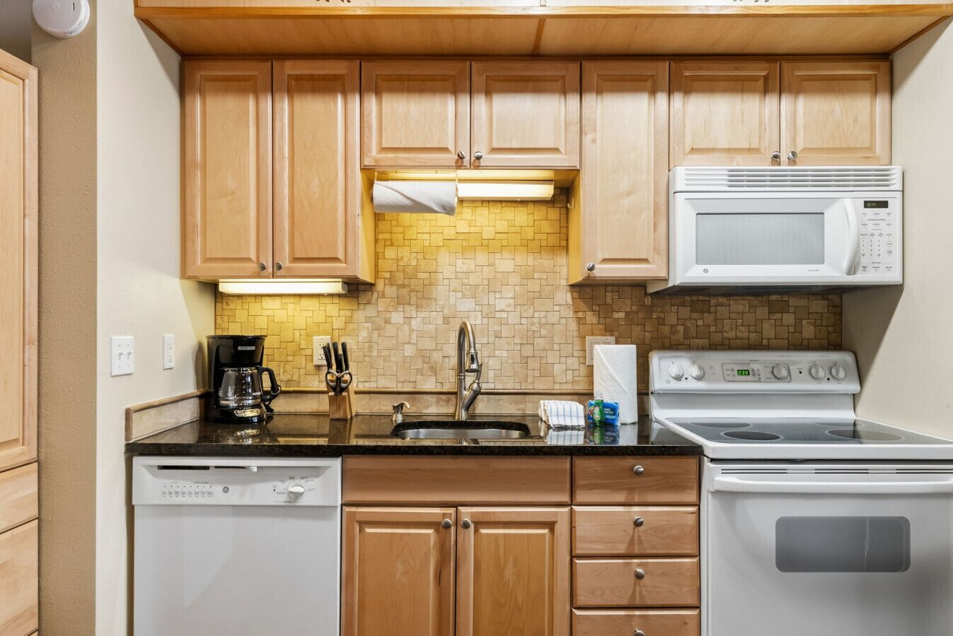 A compact kitchen with wooden cabinets, a microwave, a stove, and a dishwasher.