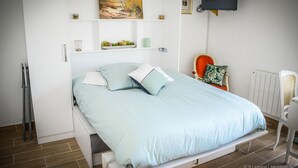 Een slaapkamer met een bed, een stoel, een televisie en een schilderij aan de muur.