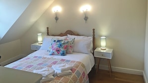Une chambre à coucher avec un plafond en pente, un cadre de lit en bois, deux lampes de chevet et une couvre-lit matelassé.