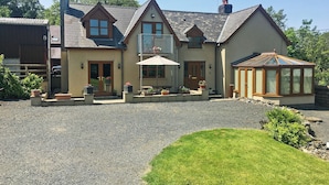 Une maison à deux étages avec un patio, une véranda et une allée gravillonnée.