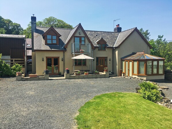 A two-story house with a patio, a conservatory, and a gravel driveway.